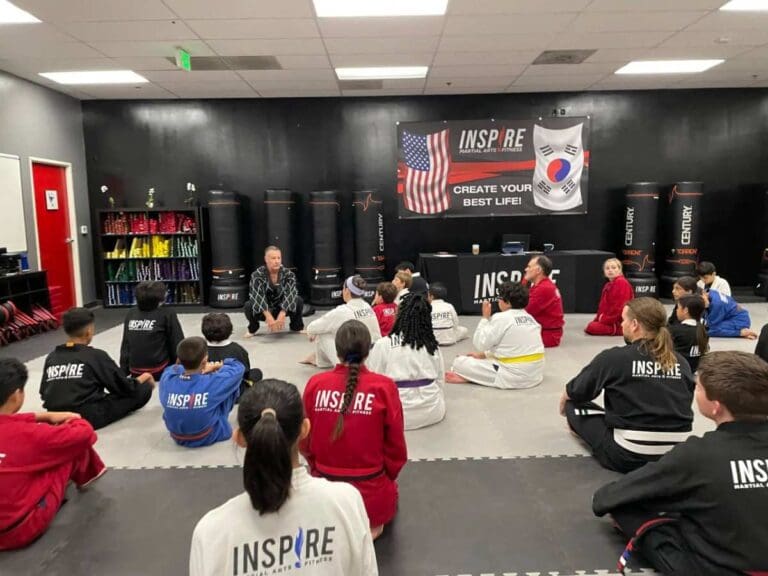 students sitting on mat listening to instructor during a self defense class